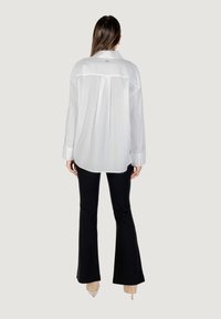 Camicia bianca con un motivo testurizzato, maniche lunghe e orlo arrotondato, abbinata a pantaloni neri aderenti.