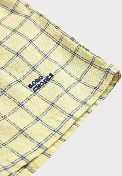 Tissu jaune à motif à carreaux bleus avec l'inscription "Bonnes Choix" brodée en fil bleu, plié sur un fond blanc.