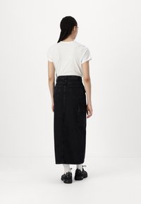Svart denim maxi skjørt med høy midje, baklommer og sidelommer, kombinert med en tettsittende hvit T-skjorte og sneakers.