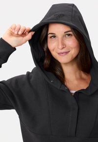 Felpa nera con cappuccio, polsi a coste, cappuccio con lacci e accento logo. Tessuto morbido e vestibilità rilassata, dotata di tasca a marsupio.