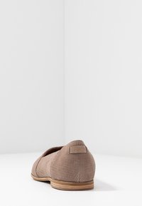 Chaussure plate perforée marron avec une surface texturée, un bout arrondi et une semelle en caoutchouc beige. Équipée d'un onglet de talon avec logo.