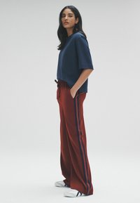 Námornícka krátke rukávové tričko skombinované s nohavicami v tehlovej farbe, ktoré majú bočné pruhy. Nohavice majú elastický pás s šnúrkou a sú nosené s bielymi teniskami.