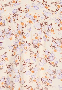 Tissu crème avec petit imprimé floral orange et violet clair, présentant des coutures froncées le long d'une couture en forme de V.