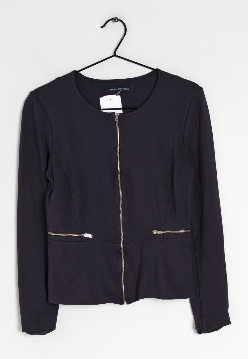 Veste noire ajustée avec un col rond, des manches longues et une fermeture éclair centrale. Comprend deux poches zippées à la taille. Texture de tissu lisse.