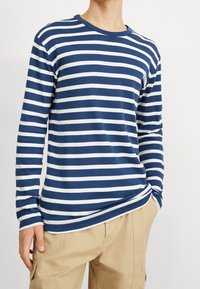 Blau- und weiß gestreiftes Langarmhemd aus weichem Stoff. Rundhalsausschnitt, enganliegende Ärmel und ein lockerer Schnitt am Saum.