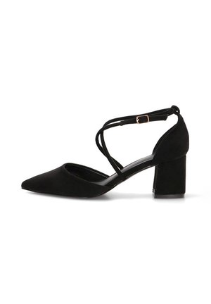 Zapato negro de ante con tacón de bloque y punta puntiaguda, con tiras cruzadas en el tobillo y una pequeña hebilla dorada sobre fondo blanco.