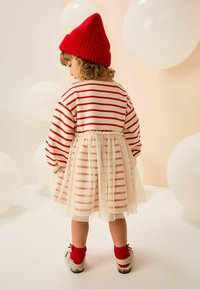 Bluză stripedă roșie și crem cu mâneci bufante, fustă din tul și fes roșu din tricot. materiale moi și texturate cu culori contrastante pe întreaga lungime.