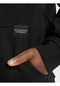 Felpa nera realizzata in un morbido misto cotone, con polsini a coste, tasca frontale e un'etichetta rettangolare nera con scritta bianca "ROCAWEAR".