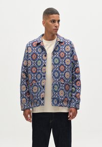 Musterjacke mit blauer Basis, die blumige Motive in Rot, Weiß, Grün und Orange zeigt. Mit Knopfleiste und zwei frontalen Taschen.