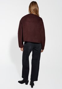 Burgundy cropped jacket with a straight silhouette, soft texture, and drop shoulders, paired with black straight-leg jeans and ankle boots.
