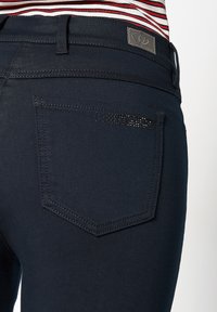 Marineblauwe denim jeans met een achterzak met een gestikte rand en strassaccenten. Gladde textuur en een slim fit ontwerp.