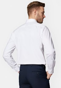 Biała koszula z długim rękawem i klasycznym kołnierzykiem, o gładkiej teksturze i mankietach zapinanych na guziki, w połączeniu z ciemnymi spodniami.