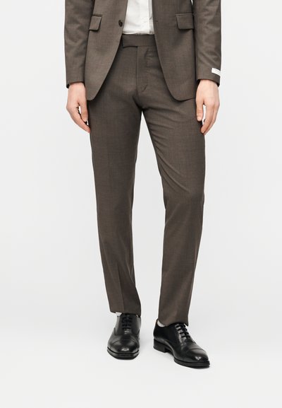 Καφέ παντελόνι κοστουμιού με υφή υφάσματος· λεπτή εφαρμογή, με ανάγλυφη ραφή μπροστά και διακριτικές πλαϊνές τσέπες, σε συνδυασμό με μαύρα επίσημα παπούτσια.