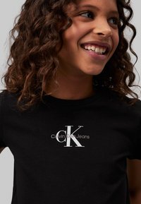 Camiseta de algodón negra con un logo blanco de Calvin Klein Jeans. Mangas cortas y cuello redondo con una textura suave y lisa.