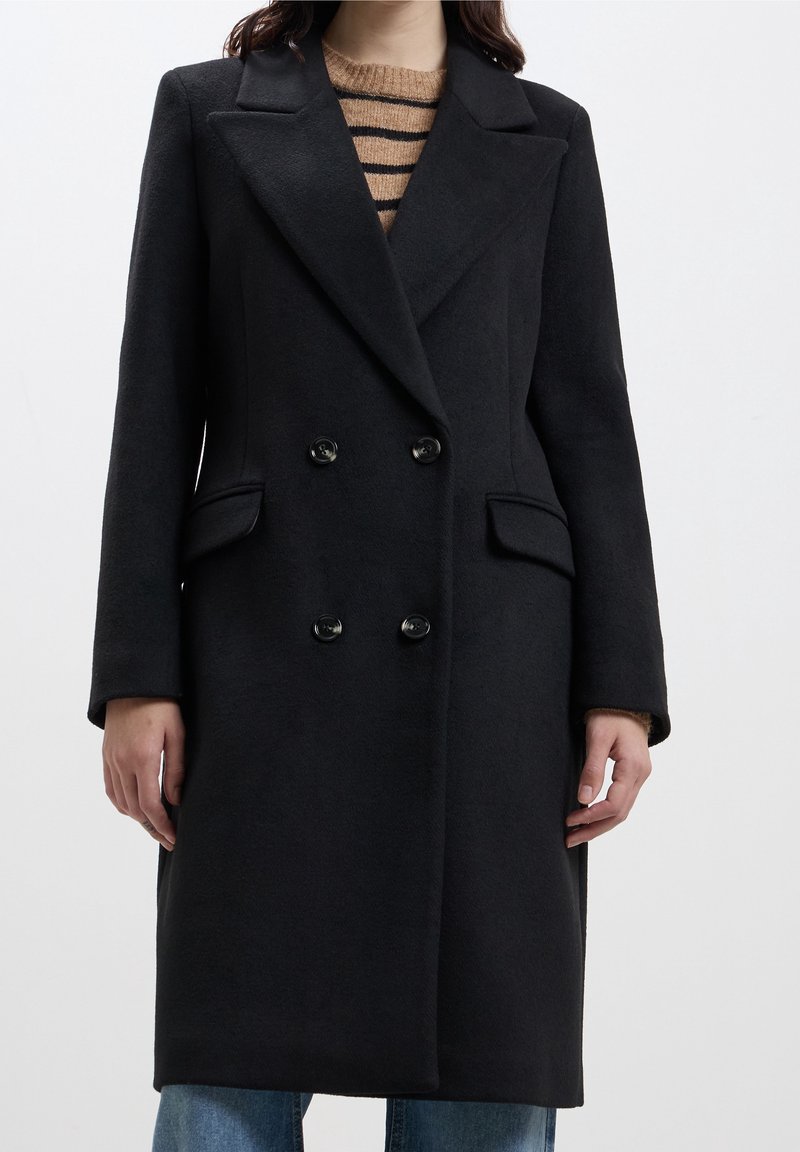 Cappotto nero doppiopetto realizzato in tessuto testurizzato, con rever a punta, due tasche frontali e bottoni a contrasto.