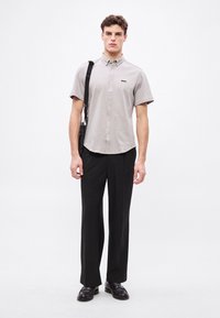 Szara koszula z krótkim rękawem z kołnierzykiem na guziki i logo, zestawiona z czarnymi, dopasowanymi spodniami i czarnymi butami. Gładka faktura tkaniny.