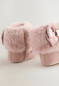 Ružové booties z falošnej kožušiny s jemnou textúrou, zaobleným tvarom a stužkovým akcentom. Obsahujú materiál podobný semišu a gumovú podrážku pre lepšiu priľnavosť.