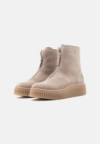 Stivali alla caviglia in suede beige con cerniera laterale, punta rotonda e suola in gomma spessa e rigata per trazione e durata.