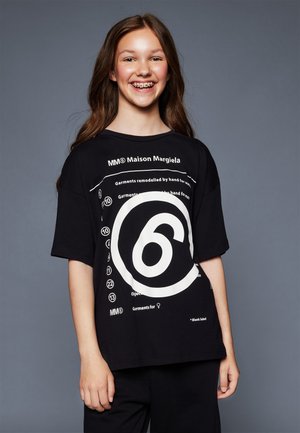 Schwarzes, übergroßes T-Shirt mit einem großen, weißen, kreisförmigen Grafik und Text, hergestellt aus weichem Stoff mit kurzen Ärmeln und einem lässigen Schnitt.
