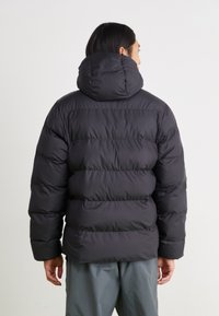 Black puffer jacket with a high collar, quilted design, and elastic cuffs, viewed from the back. Smooth texture with no visible logos.
