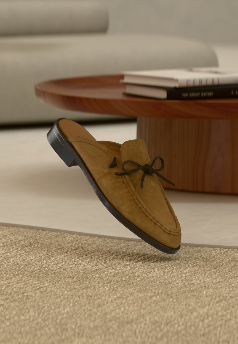 Καφέ σουέντ μοκασίνι χωρίς κορδόνια με δερμάτινη διακόσμηση φιόγκου και μαύρη ελαστική σόλα, με ραμμένα σχέδια και απαλή υφή.