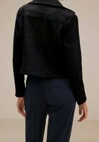 Svart imitetsläderjacka med en kort design, featuring en skräddarsydd krage och slät textur, ihop med marinblå byxor.