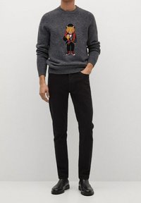 Un pull en tricot gris avec un motif de tigre en design de smoking sur la poitrine, associé à un jean noir et des bottines. Texture lisse.