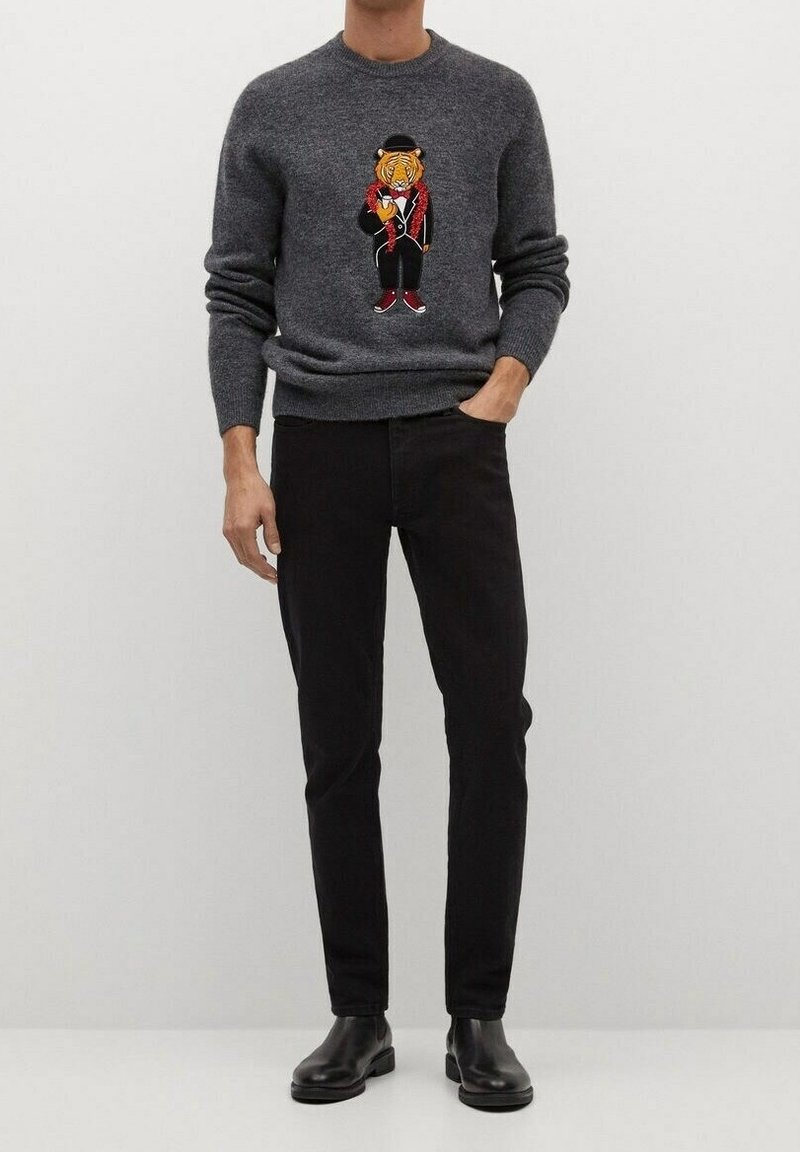 Un pull en tricot gris avec un motif de tigre en design de smoking sur la poitrine, associé à un jean noir et des bottines. Texture lisse.