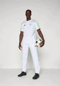 White Adidas soccer uniform with green and red accents, featuring a crew neck shirt and matching pants. Black soccer ball held in hand.