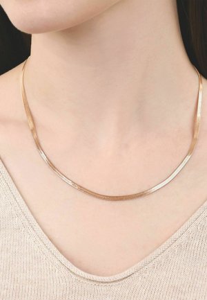 Delicate platte slangketting in roségoud gedragen om de nek van een persoon, met een beige gebreide top zichtbaar.