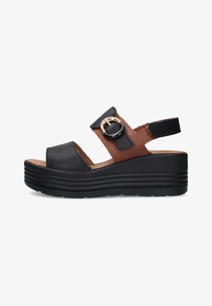 Zwarte en bruine platformsandaal met dikke zool, brede bandjes en goudkleurige ronde gesp aan de zijkant, open ontwerp van tenen en hiel.