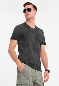 Černé tričko s výstřihem do V s texturovaným vzhledem, sešitá náprsní kapsa. Nosit s zelenými cargo šortkami a černými slunečními brýlemi.