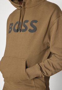Felpa con cappuccio marrone in tessuto morbido, con grande logo "BOSS" grigio sul davanti, coulisse al cappuccio e tasca anteriore.