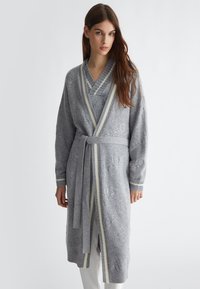 Accappatoio grigio lavorato a maglia con un motivo testurizzato, colletto a scialle e orlo a righe di colore contrastante. Include una cintura coordinata in vita.