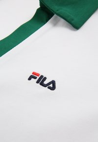 Biała koszulka polo z zielonym kołnierzykiem i paskiem. Posiada haftowane czarne logo "FILA" z czerwonym akcentem. Gładka bawełniana faktura.