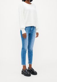 Biały sweter z dzianiny z fakturowanymi, puffowanymi rękawami, jasnoniebieskie dopasowane dżinsy i czarne loafersy na platformie z srebrnymi ćwiekami.