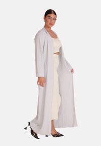 Ljusgrå lång cardigan i texturerad väv, med lös passform och breda ärmar, bärs över en krämfärgad crop top och en matchande figursydd kjol.