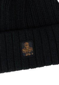 Beanie nera in maglia con texture a coste, caratterizzata da una patch rettangolare nera con una grafica dorata e testo, posizionata sul risvolto.