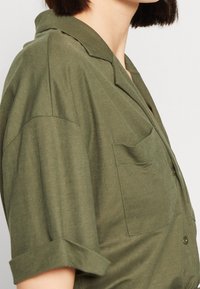 Kortärmad, olivgrön skjorta i mjukt tyg, med krage, en bröstficka och rullade ärmar med subtil textur.