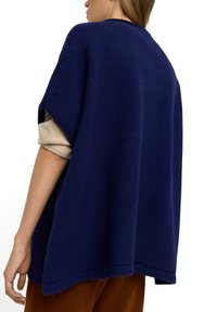 Granatowy, oversize'owy sweter o teksturowanym wykończeniu, z okrągłym dekoltem i bocznymi rozcięciami, założony na beżową bluzkę z długim rękawem.