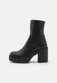 Zwarte enkelboots met een aangesloten bovenwerk, chunky plateauzool en een dikke blokhak. Gemaakt van glad leerachtig materiaal, met minimale stiksels.