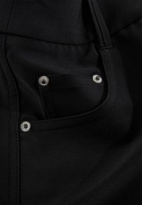 Svart tygficka med texturerad yta, utrustad med silverfärgade tryckknappar och detaljerad sömnad. Fokuserad på ren design och funktionella element.