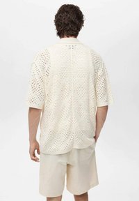 Crème opengehaakt shirt met een relaxte pasvorm, korte mouwen en een kraag, gecombineerd met lichtbeige shorts. Geweven patroon door het hele shirt.