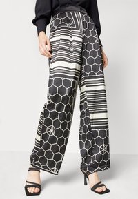 Pantalon large noir et blanc avec des motifs hexagonaux et rayés, en tissu lisse, doté d'une taille haute et de poches latérales.