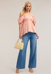 Top rosa chiaro lungo le spalle con maniche a sbuffo, vita arricciata, abbinato a jeans in denim azzurro a gamba larga e una borsa gialla con tracolla a catena.