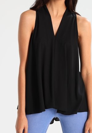 Musta hihaton pusero, jossa on V-kaula-aukko, väljä istuvuus, pehmeä kangas ja hienovarainen laskoskuvio, yhdistetty vaaleansinisiin farkkuihin.