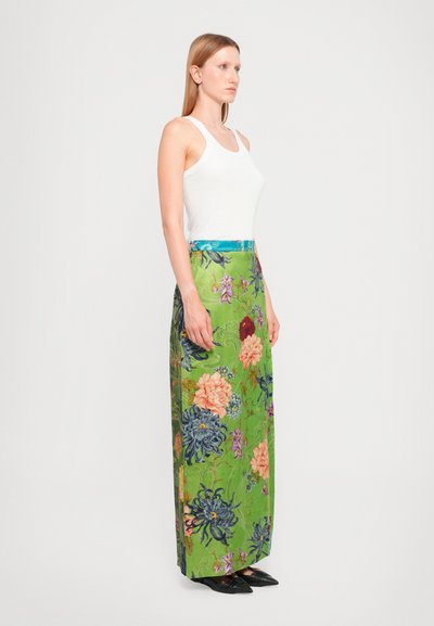 Gonna maxi floreale in tessuto verde vivace, presenta grandi fiori in rosa e blu, con una fascia in vita turchese solida. Abbinata a una canotta bianca.