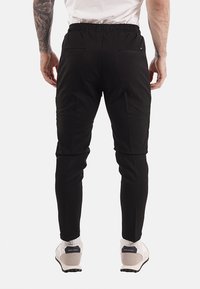 Pantalones jogger negros con cintura elástica, ajuste entallado y bolsillos traseros. La tela parece suave con un acabado mate.