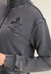 Felpa grigia scura con zip, decorata con una piccola faccia di Topolino e un testo sul petto, dettagli in strass sul petto e sul polsino delle maniche.