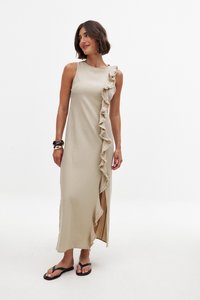 Beżowa maxi sukienka na jedno ramię z falbaną po boku. Tkanina ma teksturowany wygląd i posiada boczne rozcięcie dla swobody ruchów.